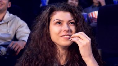 Kıvırcık saçlı neşeli bir kız loş bir sinemada kahkahalarla gülüyor ve komedi filminden zevk alıyor. Işıl ışıl gözleri ve geniş gülüşü patlamış mısırın tadını çıkartırken, etrafını film izleyicileri sarmış.