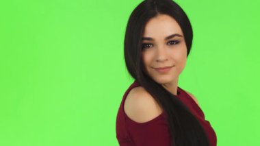 Uzun, dalgalı siyah saçlı, parlak yeşil bir fon karşısında parlak bir şekilde gülümseyen neşeli genç bir kadının çarpıcı yakın çekimi. Bulaşıcı mutluluğu pozitiflik ve güven saçıyor. Seyircileri sevinç ve kendini ifade etmeye çağırıyor.