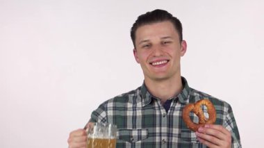 Yakışıklı, neşeli genç bir adam elinde köpüklü bir kupa bira ve lezzetli bir kraker tutarken seni kutlamaya davet ediyor. Hareketli gülüşü ve ekose gömleği canlı bir atmosfer yaratıyor. Oktoberfest festivalleri için mükemmel.