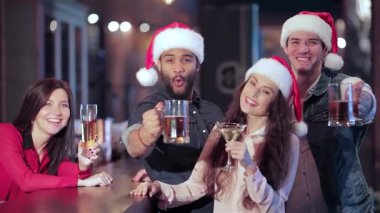 Noel Baba şapkalarıyla süslenmiş canlı bir arkadaş grubu coşkulu bir barda kadehlerini sevinçle kaldırıyor. En sevdikleri futbol takımına tezahürat ettikleri atmosfer heyecan vericidir. Yoldaşlık ve tatil neşesini somutlaştırır.