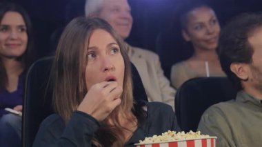 Orta yaşlı bir kadın sıcak bir sinemada oturup film büyülerken patlamış mısırın tadını çıkarıyor. İki genç kadın ve bir yaşlı adamın da dahil olduğu çeşitli izleyicilerle çevrili ortamda heyecan ve neşe hakim.
