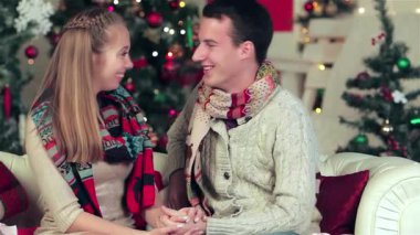 Sıcak, Noel dekore edilmiş bir odada, sıcak kazaklar ve renkli eşarplar giymiş büyüleyici bir çift sevgi dolu hediyeler vererek hassas bir anı paylaşıyorlar. Işıl ışıl gülümsemeleri ve şefkatli bakışları büyüleyici bir atmosfer yaratır.