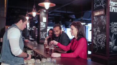 Aralarında iki neşeli kadın ve bir erkeğin de bulunduğu canlı bir yetişkin grubu, geceyi barda kahkahalar ve içkilerle kutluyor. Barmen ustalıkla tazeleyici biraları servis eder. Arkadaşları da en sevdikleri futbol takımına tezahürat eder.