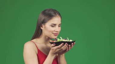 Çekici, sağlıklı, uzun saçlı bir kadın parlak siyah bir kasede canlı bir salatanın enfes kokusunu içine çekerken mutlu bir şekilde gülümsüyor. Bu büyüleyici an neşe saçıyor ve besleyiciliğin güzelliğini gösteren sağlıklı bir yaşam tarzını teşvik ediyor.