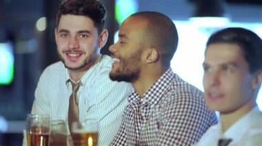 Dört neşeli iş adamı, TV 'deki futbol maçının heyecanıyla kadeh kaldırarak bira kadehlerini kaldırıyor. Titreşimli atmosfer kahkaha ve dostlukla dolu, bu hareketli barda birbirlerine eşlik etmekten hoşlanıyorlar.