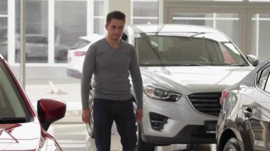 Şık bir genç adam modern bir otomobil galerisinde parıldayan model arabaları karıştırıyor, heyecan ve merak saçıyor. Dost canlısı bir satıcıya rastladığı için, parlak, parlak çevre araba alışverişinin heyecanını arttırıyor.