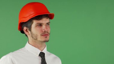 Yakışıklı bir genç adam portresi, bakımlı sakallı, parlak turuncu bir şapka takıyor ve beyaz bir gömlek giyiyor, düşünceli bir şekilde uzaktan bakıyor. Düşünceli ifadesi, canlı bir kromakey arka plan, bir çağrıştırır