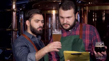 İki yetenekli erkek bira imalatçısı, biri sakallı, zanaat biralarını yakından inceliyor, canlı bir altın bira ve zengin koyu bir bira sergiliyor. Hareketli bir tartışmayla, takım çalışmasının ruhunu somutlaştırdılar ve demleme sanatında kendilerini adadılar.