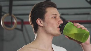 Canlı yeşil bir şişeden neşeyle su yudumlayan genç, zinde bir adamın yakından çekilmiş portresi fitness 'e olan bağlılığını gösteriyor. Işıl ışıl gülüşü ve gevşek tavırları başarılı bir eğitim seansının memnuniyetini yansıtıyor.