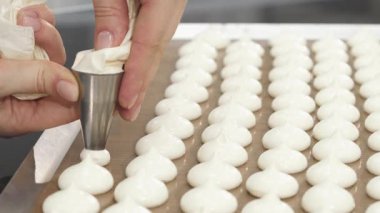 Becerikli bir şekerci titizlikle narin kurabiyeleri mükemmel sıralarda, hassas ve sanatsal olarak sergiliyor. Krem şantiden parlak beyaz tepeler hoş bir ikram vaat ediyor, tatlı bir beklenti yaratıyor.