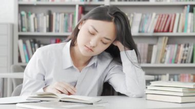 Yorgun, genç bir Asyalı kadın, huzurlu bir kütüphanede kitap yığınlarıyla çevrili bir çalışma masasında uykuya dalıyor. Sahne, akademik baskının mücadelesini kafasının elinde dinlenerek, gece geç saatlerdeki çalışmanın yorgunluğunu somutlaştırarak yakalıyor.