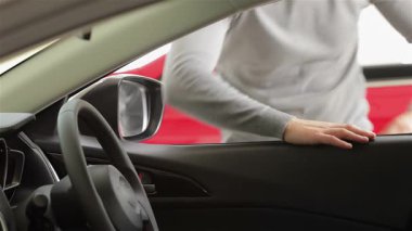 Genç bir adam, tasarımı ve özellikleri karşısında büyülenen modern bir aracın lüks iç mekanına hevesle eğilir. Bu canlı sahne araba alışverişinin heyecanını yakalıyor, müşteriyle bilgili bir satıcı arasındaki bağlantıyı gözler önüne seriyor.