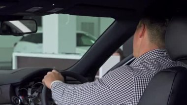 Neşeli bir adam, yeni bir galeride lüks bir arabada otururken, heyecan saçarak, omzunun üzerinden başparmağını kaldırıyor. Bu canlı sahne, yeni bir otomobil seçmenin heyecanını yakalıyor, modern tüketim zevkini ve cazibesini somutlaştırıyor.