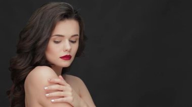 Çıplak omuzlu zarif bir genç kadın kameraya özgüvenle bakıyor, çarpıcı kırmızı dudakları ve parlak siyah bir arka planda yüzünü çerçeveleyen yumuşak kıvırcık saçları. Bu büyüleyici portre onun kusursuz cildini ve zarif davranışlarını vurguluyor.