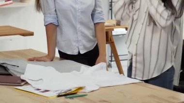 Canlı bir sahne, biri bir tişörtü ustalıkla katlarken diğerinin gözlemlediği şık bir giyim mağazasında işbirliği yapan iki odaklanmış kadın tasarımcıyı yakalıyor. Bu canlı atmosfer moda ve takım çalışmasına olan tutkularını gözler önüne seriyor.