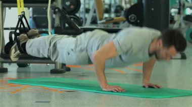 Orta Doğulu etnik kökenli odaklanmış genç bir adam canlı yeşil bir minder üzerinde güçlü şınav çekiyor, fitness ve güç eğitimine olan bağlılığını gösteriyor. Spor salonu enerji ile uğulduyor, çeşitli spor ekipmanlarıyla birlikte...