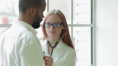 Parlak bir klinikte, odaklanmış bir kadın doktor steteskopla genç bir adamın göğsünü dinler ve kapsamlı bir muayene sağlar. Sıcak gülüşü ve mesleki tavırları onun için reçete yazmaya hazırlanırken rahatlatıcı bir atmosfer yaratıyor.