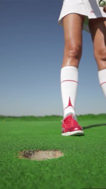 Büyüleyici bir yakın çekim, şık bir beyaz etek ve tişört giymiş kararlı beyaz bir beyaz kadın, golf topuna canlı yeşil bir sahada vurmaya hazırlanıyor. Işıl ışıl yaz güneşinin altında, atletizmi ve hassasiyeti ışıldıyor