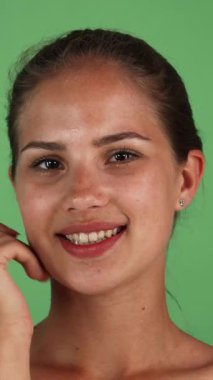 Işıl ışıl cildi parlayan neşeli bir genç kadın, eli yavaşça yanağını yeşil bir zemine sürterek gülümsüyor. Bu büyüleyici portre pozitiflik ve güzellik saçıyor, gençlik parıltısını ve zahmetsiz çekiciliğini vurguluyor.