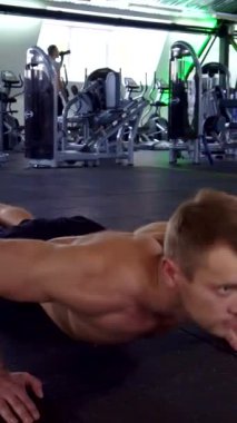 Kendini işine adamış genç beyaz bir adam, etkileyici kaslı yapısını sergileyerek, parlak, siyah bir spor salonuna odaklanarak şınav çekiyor. Yoğun ifadesi kararlılık ve disiplin yayıyor. Gücün özünü somutlaştırıyor.