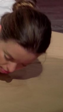 Saf mutluluğa kapılmış dingin genç bir kadın, yetenekli bir pratisyen nazikçe sırtını gererken geleneksel Tayland masajını tecrübe eder. Yumuşak ışıklandırma ve zengin kırmızı aksanlarla süslenmiş huzurlu spa ortamı, terapi gücünü arttırır.