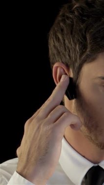 Gıcır gıcır beyaz gömlekli, parlak siyah kravatlı, ciddi bir beyaz adam kulaklığından dikkatlice dinliyor elini kulağına doğru kaldırıyor. Dramatik siyah arkaplan onun komuta gücünü arttırıyor, modern bir görünüm çağrıştırıyor.