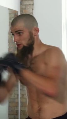 Odaklanmış sakallı bir erkek dövüşçü pedere sert bir yumruk sallıyor, canlı bir spor salonunda ham güç ve hassasiyet sergiliyor. Bu heyecan verici an, takım çalışmasının ruhunu somutlaştırıyor ve amansız bir adanmışlık ve yoğun bir şekilde...