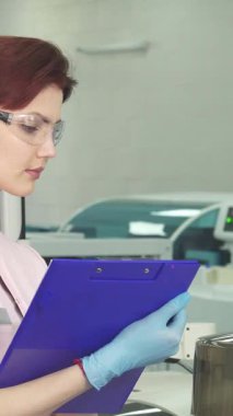 Koruyucu gözlük ve mavi eldiven takan kendini işine adamış kızıl saçlı bir kadın bulgularını karmaşık laboratuvar ekipmanlarının arasında canlı mavi bir panoya kaydediyor. Onun sarsılmaz odağı ve araştırma tutkusu bu modern bilimi aydınlatıyor.