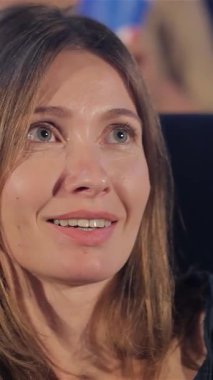 Neşeli yetişkin bir kadının yakın çekimi, bir komedi filminin mizahıyla eğlenirken karanlık tiyatroyu aydınlatan parlak gülüşü. Bu güzel beyaz kadın saf mutluluğun simgesi, sinemanın büyüsünü yakalıyor ve kahkahaların ortak deneyimini yaşıyor.