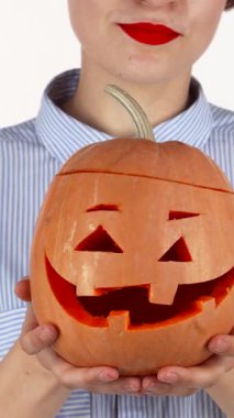 Çarpıcı kırmızı dudakları olan neşeli bir kadın tuhaf bir şekilde oyulmuş bir Cadılar Bayramı balkabağı sunarken ışıl ışıl parlıyor. Bu canlı sahne, sonbahar şenliklerinin ruhunu özetliyor. Sıcaklık ve heyecan yayıyor.