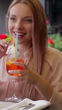 İki ışıl ışıl kadın güneşin tadını çıkarıyor, çiçeklerle süslenmiş büyüleyici bir terasta kahkahalarını ve renkli kokteyllerini paylaşıyorlar. Canlı kavuşmaları arkadaşlığın neşesini özetliyor. Sıcak ve sıcak bir yaz ortamı yaratıyor.