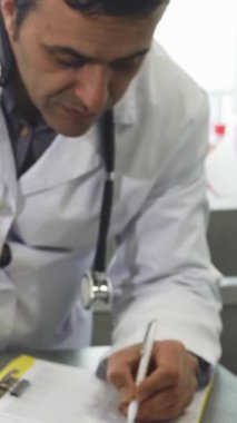 Sevimli bir Boston teriyeri yavrusu sınav masasında gururla durup kameraya merakla bakarken yetişkin bir erkek veteriner arka planda özenle evrak dolduruyor. Bu iç açıcı sahne güzel bir şekilde...