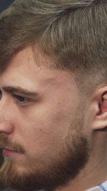 Bu yakın plan, yetenekli bir berber saçını elektrikli makasla titizlikle şekillendirirken kendine güveni yayan yakışıklı bir genci gösteriyor. Modern dekor ve enerjik enerjiyle dolu şık bir berber dükkanı ortamı, sanatın ve