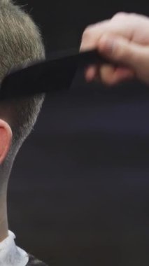 Bu yakın plan çekimde, yetenekli bir berber saçını elektrikli makasla titizlikle budarken kendine güveni yayılan yakışıklı genç bir adam sergileniyor. Şık berber dükkanı, modern tımarcılığın sanatını ve hassasiyetini vurgulayan canlı bir atmosfer yayar.