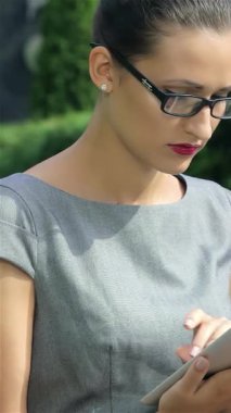 Gösterişli gri bir elbise giymiş kararlı bir işkadını, tabletindeki verileri dikkatle analiz ederek, modern profesyonelliğin özünü somutlaştırıyor. Şık gözlükleri ve kendine güveni, yemyeşil bir zemin üzerine kurulmuş, çarpıcı bir hava yaratır.