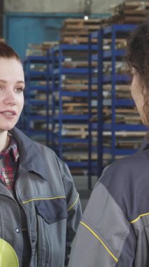 Parlak bir tebessüm ve şapkayla süslenmiş, hayat dolu genç bir depo çalışanı meslektaşı ile hareketli bir metal deposunun ortasında hareketli bir sohbete dalıyor. Bu canlı sahne güzel bir şekilde resmediyor.