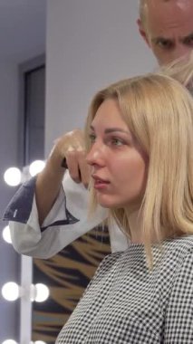 Şık bir kuaförde saçları yetenekli bir kuaför tarafından değiştirilirken ışıl ışıl gülümseyen genç bir kadın. Parlak ışıklar ve modern dekor davetkar bir atmosfer yaratarak bu lüks şımartıcı deneyimin neşesini arttırıyor.