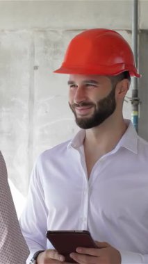 Gıcır gıcır beyaz gömlekli ve parlak turuncu şapkalı genç, sakallı bir inşaat mühendisi bir meslektaşıyla hareketli bir inşaat alanındaki takım çalışmasının ruhunu somutlaştıran canlı bir tartışmaya girişiyor. İnceleme sırasında hava enerjiyle doludur.