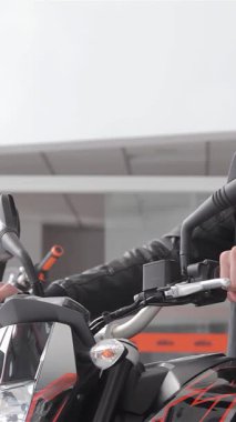 Beyaz sakallı, şık, genç, beyaz bir adam, özgüven ve karizma saçan, parlak siyah bir motorsikletin benzin deposuna rahatça yaslanıyor. Ekose gömlek ve klasik deri ceket giyip modern bir maceranın ruhunu somutlaştırıyor.