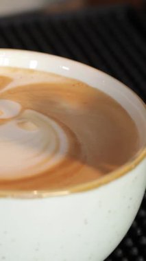 Yetenekli bir erkek barista, sıcaklığı yayıyor, titizlikle kremalı köpüğü döküyor, canlı bir kahve tezgahının üstünde sersemletici bir latte sanatı yaratıyor. Davetkar atmosfer taze demlenmiş espressonun aromatik kokusuyla dolu.