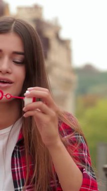 İki ışıl ışıl genç kadın, biri uzun kahverengi saçlı, diğeri dalgalı koyu saçlı, coşkulu bir şehir caddesinde köpüklü sabun köpükleri üflüyor. Bulaşıcı kahkahaları havada dans eder, kaygısız bir yaz gününün özünü yakalar.