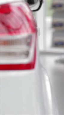 Rahat bir süveter içinde şık bir genç kadın parlak, modern bir bayilikte şık bir model arabayı inceliyor ve otomotiv tercihleri için heyecan saçıyor. Parlak araçlar ve çağdaş tasarım ile dolu canlı atmosfer onu güçlendiriyor.