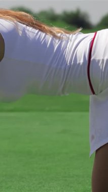 Büyüleyici bir yan bakış, dört ayak üzerinde duran kızıl saçlı çarpıcı bir golfçüyü yakalıyor ve vurmaya hazırlanırken deliğe odaklanıyor. Pürüzsüz beyaz bir etek ve üzerine de bir tişört giymiş olan bu beyaz atletik kadın yaz sporu enerjisi yayıyor.