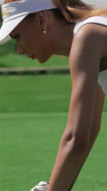 Büyüleyici bir yan bakış, dört ayak üzerinde duran kızıl saçlı çarpıcı bir golfçüyü yakalıyor ve vurmaya hazırlanırken deliğe odaklanıyor. Pürüzsüz beyaz bir etek ve üzerine de bir tişört giymiş olan bu beyaz atletik kadın yaz sporu enerjisi yayıyor.