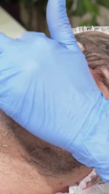 Kendini işine adamış bir kozmetikçi, zengin bir karbon maskesini rahatlamış bir erkek müşteriye ustalıkla uygular ve onun canlandırıcı yüz deneyimini geliştirir. Huzurlu klinik atmosferi, müşterilerin huzurlu gülümsemeleriyle eşleştirildiğinde, dönüşümsel etkilerin