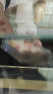 Neşeli genç bir fırıncı kız fırın tezgahından renkli makaronlar sergiliyor. Sıcak kahve dükkanının davetkar atmosferi taze hamur işlerinin tatlı kokusuyla dolu. İstekli müşteriler için sıcak bir cennet yaratıyor.