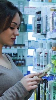 Sıcak bir gülümsemesi olan keyifli genç bir kadın hareketli bir eczanede renkli sağlık ve güzellik ürünlerini inceliyor. Bu canlı sahne perakende terapi titreşimleri yayıyor, sağIık yolculuğu için mükemmel ürünleri seçerken heyecanını vurguluyor.