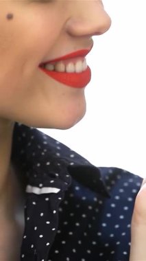 Çarpıcı kırmızı dudakları olan neşeli bir kızın büyüleyici bir yakın çekimi, üzerine canlı serpiştirilmiş renkli bir donut tutuyor. Eski saç stili ve neşeli ifadesi hoş bir nostalji hissi uyandırıyor, çekiciliği somutlaştırıyor.