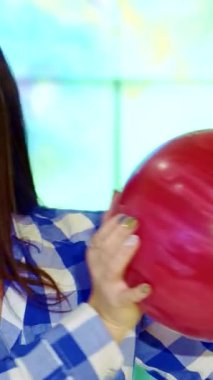 Neşeli esmer bir kız yüzüne çarpan kırmızı bir bovling topunu neşe ve coşku saçarak şakacı bir şekilde beşiğinde tutuyor. Bu yakın plan çekimde, şık mavi ve beyaz kareli gömlekli neşeli beyaz bir kadın, eğlence dolu bir gömlek için mükemmel hazırlanmış,