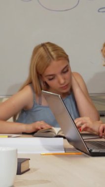 Kameraya neşeli bir bayan öğrenci ışıldıyor, altın rengi saçları sınıf arkadaşlarıyla çarpışırken, dizüstü bilgisayarlarına ve notlarına dalmış. Bu canlı sahne, parlak bir şekilde hazırlanan işbirliği ve öğrenme hevesini yayıyor.